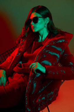 Kırmızı ceketli zarif trend bayanın moda portresi. Neon ışığı, güneş gözlüğü, stüdyo çekimi.