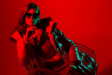 Kırmızı ceketli zarif trend bayanın moda portresi. Neon ışığı, güneş gözlüğü, stüdyo çekimi.