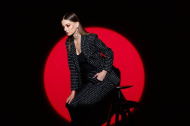 Siyah takım elbiseli bezelyeli genç bir kadının moda portresi. Kırmızı arkaplan, spot ışığı, eski tarz 