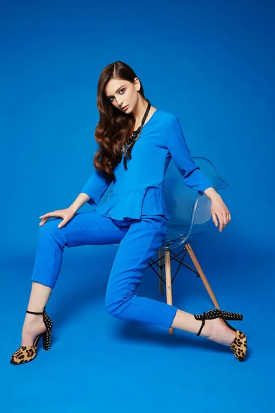 若いエレガントな女性の高ファッションの肖像画 青いブラウス 青いパンツ 巻き毛 ヒョウの靴 青の背景 — ストック写真