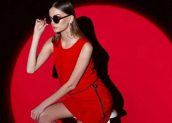 赤いドレスで若い女性のファッションの肖像画 サングラス 赤い背景 スポットライト — ストック写真
