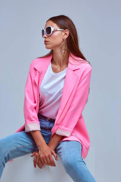 若いエレガントな女性のファッションの肖像画 ピンクのジャケット 青いジーンズ サングラス スタジオショット — ストック写真