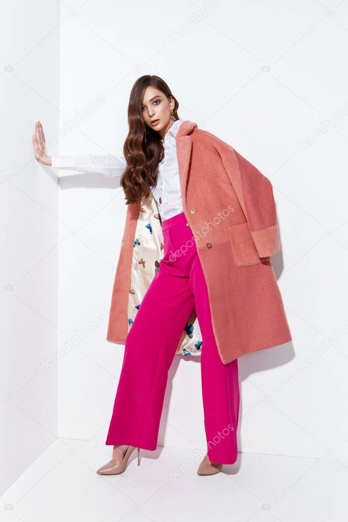 High fashion portrait of young elegant woman. Coral coat, magenta pants, white blouse. White background