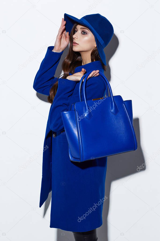High fashion portrait of young elegant woman. Blue coat, hat, bag. White background