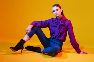 Genç ve zarif bir kadının yüksek moda portresi. Sudio çekimi. Mor bluz, mavi pantolon, ayak bileği botları, sarı arka plan