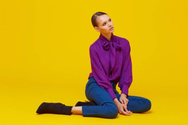 Genç ve zarif bir kadının yüksek moda portresi. Sudio çekimi. Mor bluz, mavi pantolon, ayak bileği botları, sarı arka plan