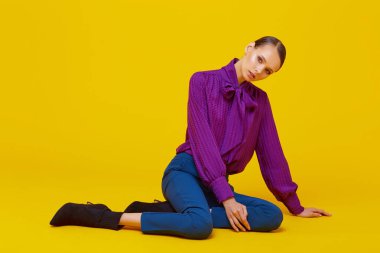 Genç ve zarif bir kadının yüksek moda portresi. Sudio çekimi. Mor bluz, mavi pantolon, ayak bileği botları, sarı arka plan