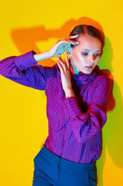 Genç ve zarif bir kadının yüksek moda portresi. Sudio çekimi. Mor bluz, mavi pantolon, ayak bileği botları, sarı arka plan