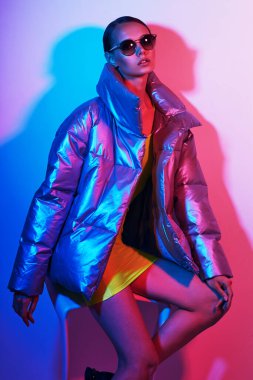 Güneş gözlüklü zarif bir kadının moda portresi. Gümüş rengi ceketli, neon ışıklı