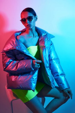 Güneş gözlüklü zarif bir kadının moda portresi. Gümüş rengi ceketli, neon ışıklı