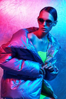 Güneş gözlüklü zarif bir kadının moda portresi. Gümüş rengi ceketli, neon ışıklı