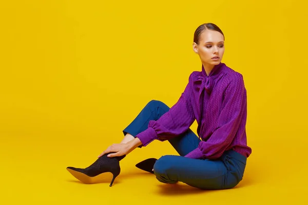 High fashion portrait of young elegant woman. Sudio shot. Violet blouse, blue pants, ankle boots, yellow background