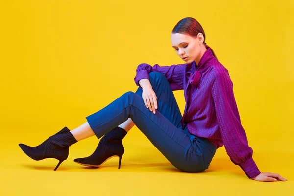 若いエレガントな女性の高ファッションの肖像画 スタジオで撃たれた 紫のブラウス 青いパンツ 足首のブーツ 黄色の背景 — ストック写真