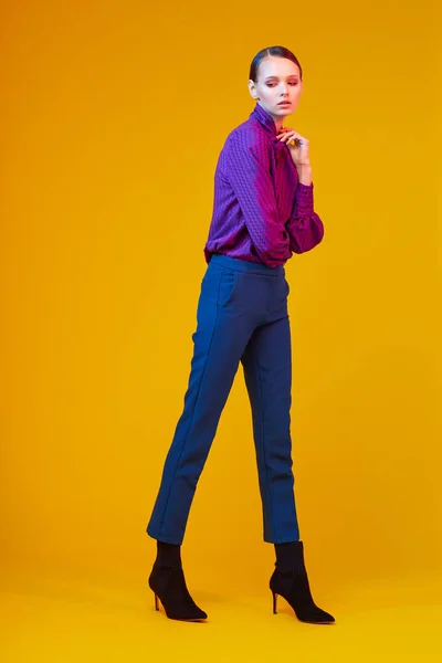 年轻优雅女子的高级时尚肖像 苏迪欧开枪了紫罗兰衬衫 蓝色裤子 脚踝靴 黄色背景 — 图库照片