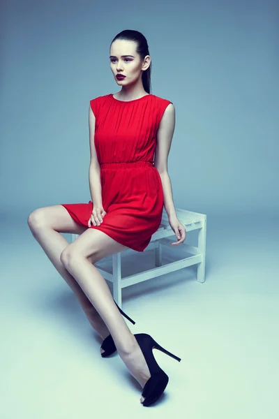 Junge elegante Frau im roten Kleid sitzt auf Hocker, Studioaufnahme — Stockfoto