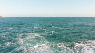 Mavi okyanus, köpüklü dalga ve açık mavi gökyüzü ile güzel bir deniz manzarası.