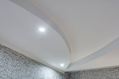 Karmaşık kartonpiyerli tavan ayrıntıları. Apartmanda ya da evde boş bir odada asılmış tavan ve alçıpan inşaatı. Gergin tavan beyaz ve karmaşık şekil.