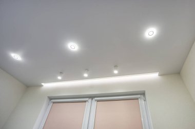 Halojen lambalı asma tavan ve boş bir oda ya da evde alçıpan inşaatı. Gergin tavan beyaz ve karmaşık şekil.