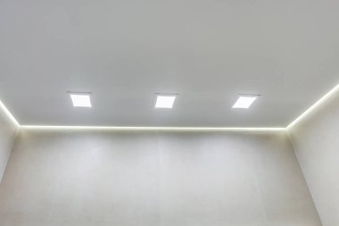 Halojen lambalı asma tavan ve boş bir oda ya da evde alçıpan inşaatı. Gergin tavan beyaz ve karmaşık şekil.