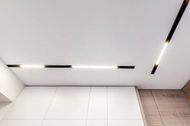 Halojen lambalı asma tavan ve boş bir oda ya da evde alçıpan inşaatı. Gergin tavan beyaz ve karmaşık şekil.