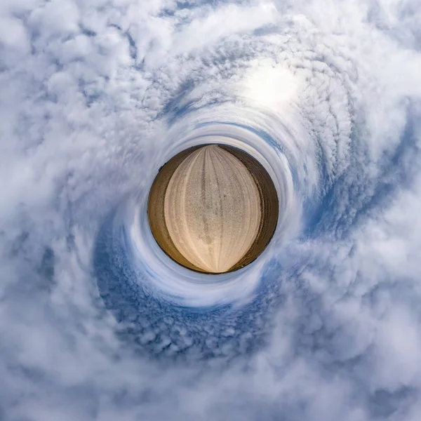 tiny planet in blue sky with sun and beautiful clouds. Transformation of spherical panorama 360 degrees. Spherical abstract aerial view. Curvature of space.