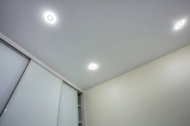 Halojen lambalı asma tavan ve boş bir oda ya da evde alçıpan inşaatı. Gergin tavan beyaz ve karmaşık şekil.