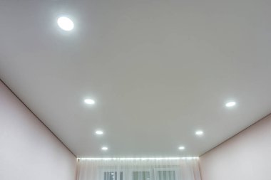 Halojen lambalı asma tavan ve boş bir oda ya da evde alçıpan inşaatı. Gergin tavan beyaz ve karmaşık şekil.