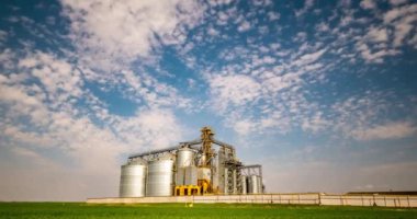 Time lapse of modern granary elevator against the blue sky. Silver silos on agro-processing and manufacturing plant for processing drying cleaning and storage of agricultural products.