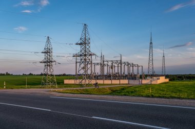 Güzel akşam bulutlarının arkasındaki yüksek voltajlı elektrik kulelerinin silueti.