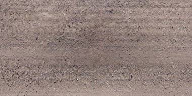 Çakıl yolu yüzeyinde yol manzarası ve araba lastiği izleri var.