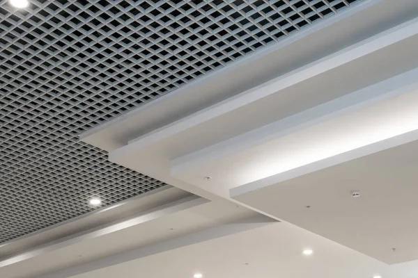 suspended and grid ceiling with halogen spots lamps and drywall construction in empty room in store or house. Stretch ceiling white and complex shape.