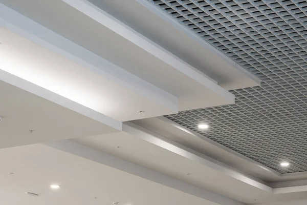 suspended and grid ceiling with halogen spots lamps and drywall construction in empty room in store or house. Stretch ceiling white and complex shape.