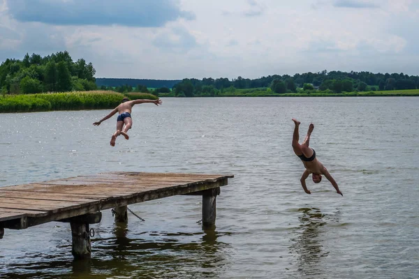 Erkeklerin silueti, tahta iskelenin yakınındaki gölün suyuna dalıyor.
