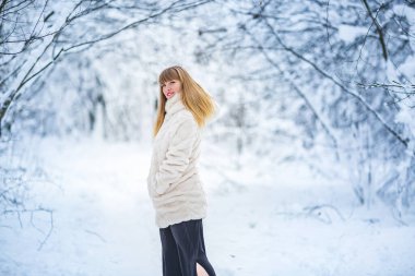Güzel, kendine güvenen, beyaz kürklü güzel bir kadın. Karlı ormanda yalnız poz veren kameraya bakıyor.