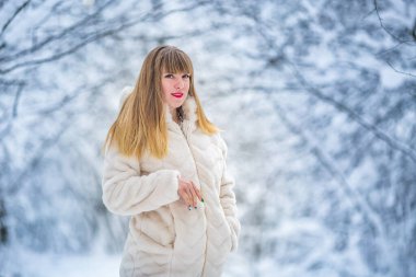Güzel, kendine güvenen, beyaz kürklü güzel bir kadın. Karlı ormanda yalnız poz veren kameraya bakıyor.