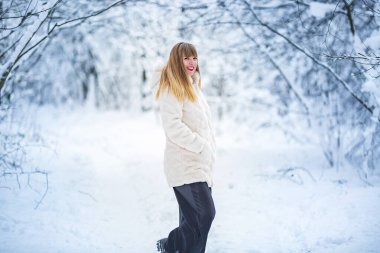 Güzel, kendine güvenen, beyaz kürklü güzel bir kadın. Karlı ormanda yalnız poz veren kameraya bakıyor.
