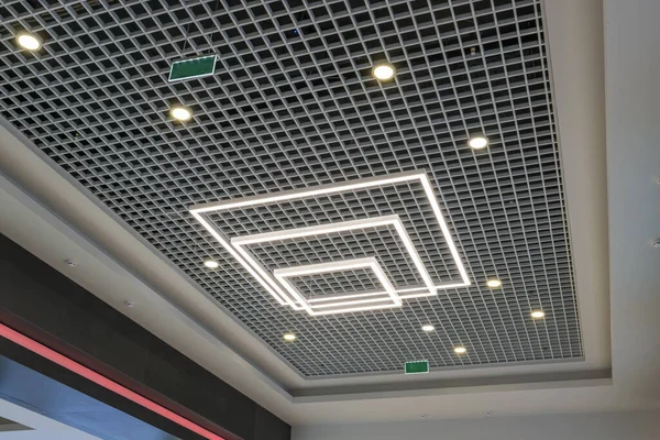 suspended and grid ceiling with halogen spots lamps and drywall construction in empty room in store or house. Stretch ceiling white and complex shape.