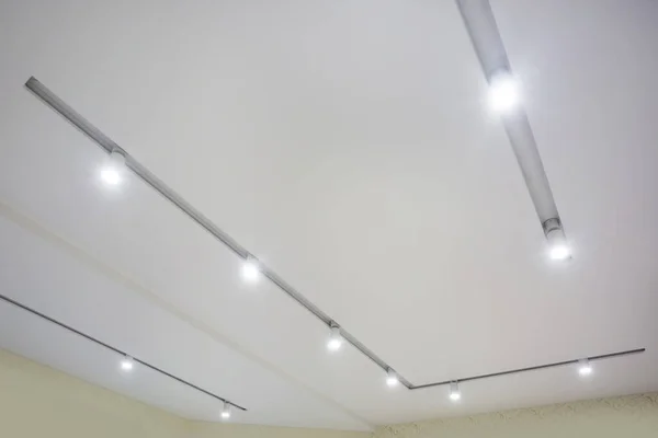 suspended ceiling with halogen spots lamps and drywall construction in empty room in apartment or house. Stretch ceiling white and complex shape.