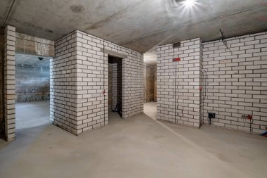 Beyaz tuğlalı duvarlarla iç mekanda minimum hazırlık onarımı yapılmış boş bir bodrum odası.