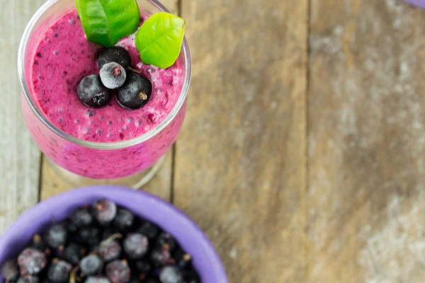 Milkshake med svarta vinbär i ett glas mot bakgrund av träskivor — Stockfoto