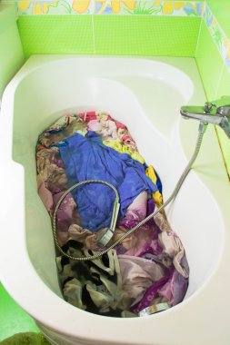 Dirty clothes soak in tub with detergent before washing clipart