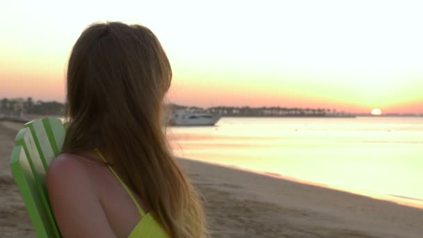 Meisje ligt op een strandstoel bij zonsondergang. HD — Stockvideo