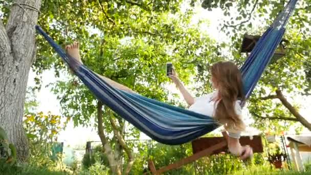 Vacker flicka liggande i en hängmatta och gör selfie. HD — Stockvideo