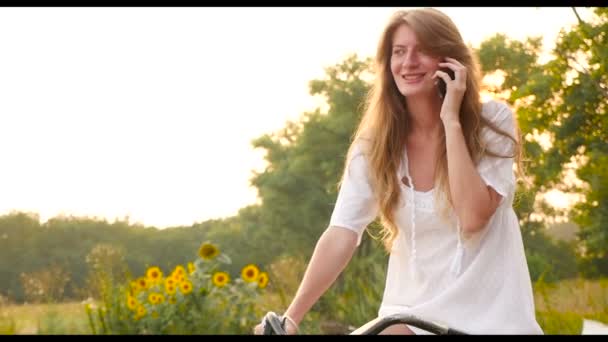 Uma menina senta-se em uma bicicleta e falando ao telefone . — Vídeo de Stock