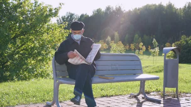 Senior man met gezichtsmasker en bril die krant leest zittend op bank — Stockvideo