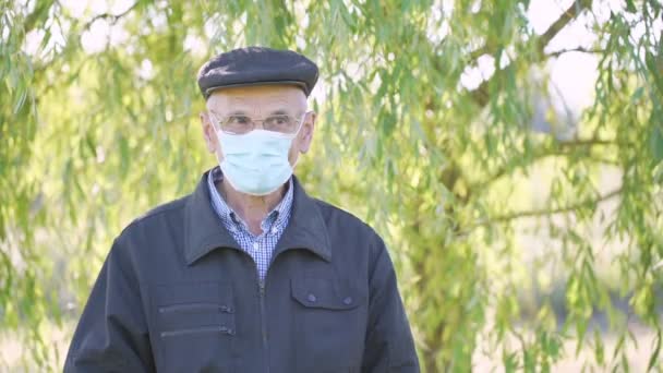 Porträtt av äldre man bär mössa och medicinsk ansiktsmask i stadsparken — Stockvideo