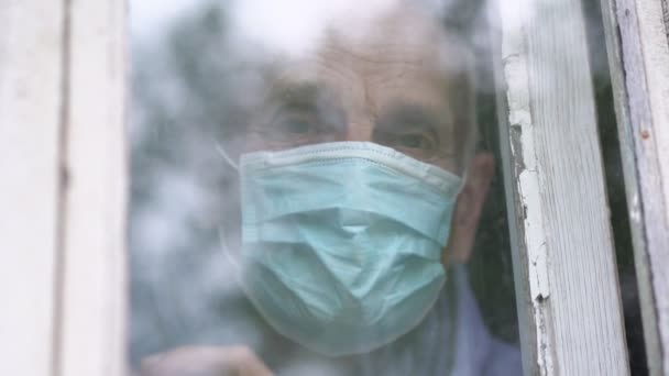 Homem sênior usando máscara facial mostrando gesto do coração por mãos ficar em casa na janela — Vídeo de Stock