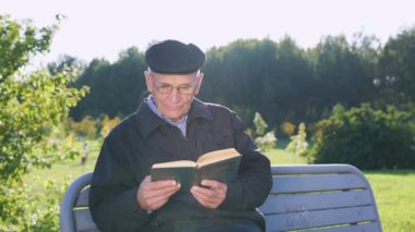 Son sınıf öğrencisi şapkalı ve gözlüklü kitap okuyor parkta bankta oturuyor.