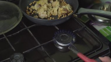 Yaşlı adam gaz ocağında ateş yakıyor ve tavaya pirinç ve etle yağ döküyor.