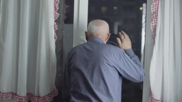 窓から見て手をロックダウンの概念で手を振る顔マスクの男 — ストック動画